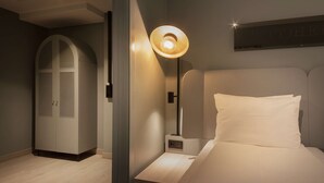 Un dormitorio con cama, mesita de noche, lámpara, armario y un cartel en la pared.