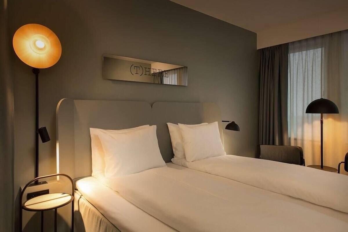 A hotel room with a large bed, two bedside tables, a wall-mounted mirror, and a window with curtains.