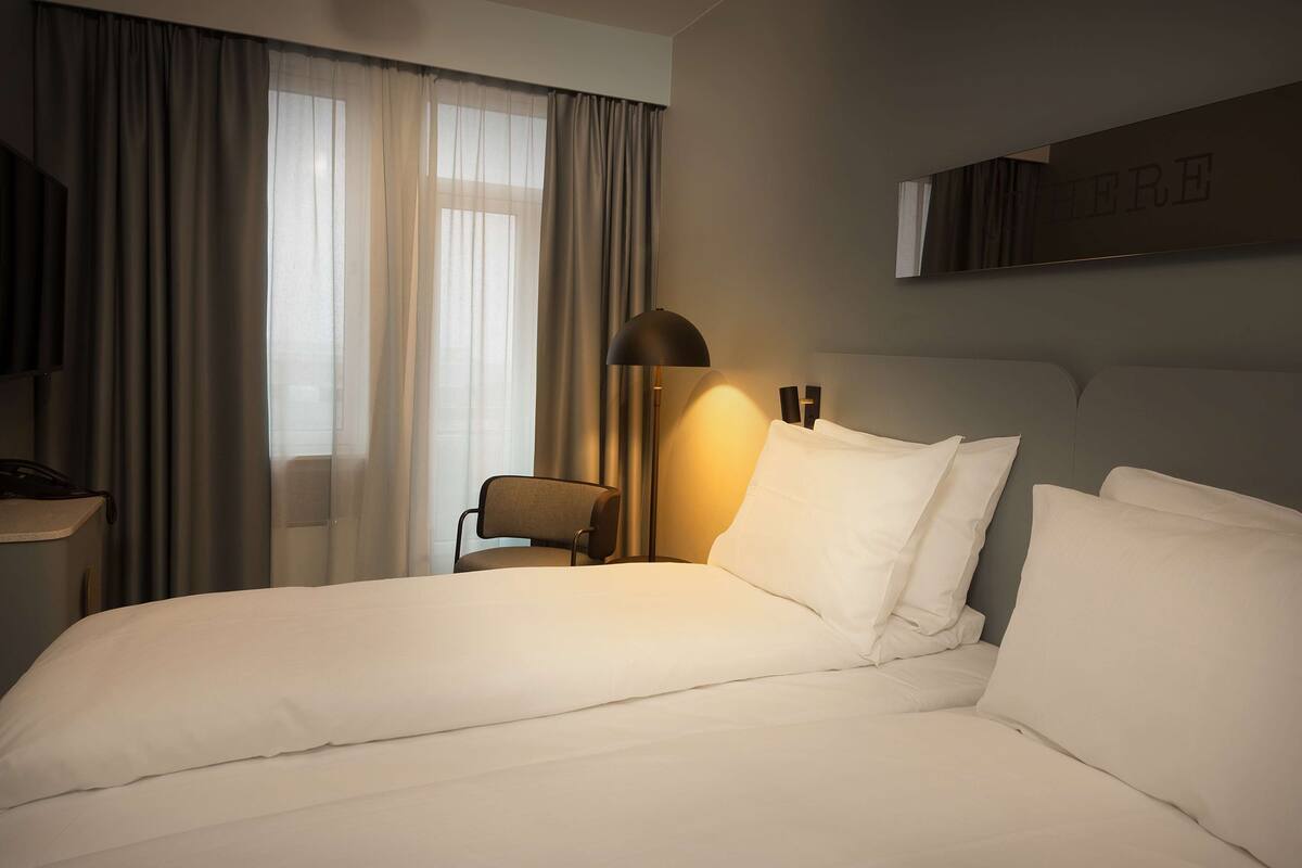 A hotel room with a large bed, a chair, a desk with a lamp, and a sign on the wall.