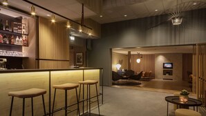 Un moderno bar con taburetes, una barra repleta de botellas y una zona de estar con televisor.