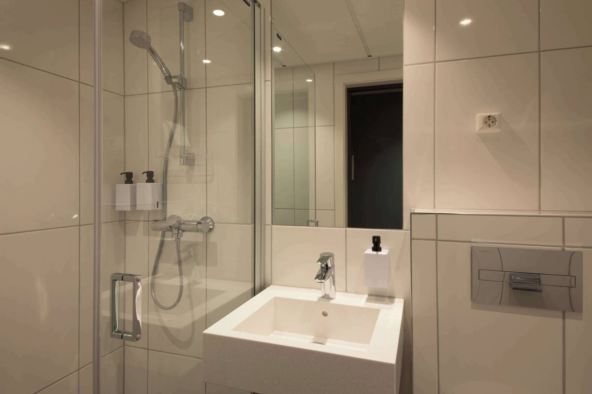 A modern bathroom with a glass-enclosed shower, a white sink, and a mirror.