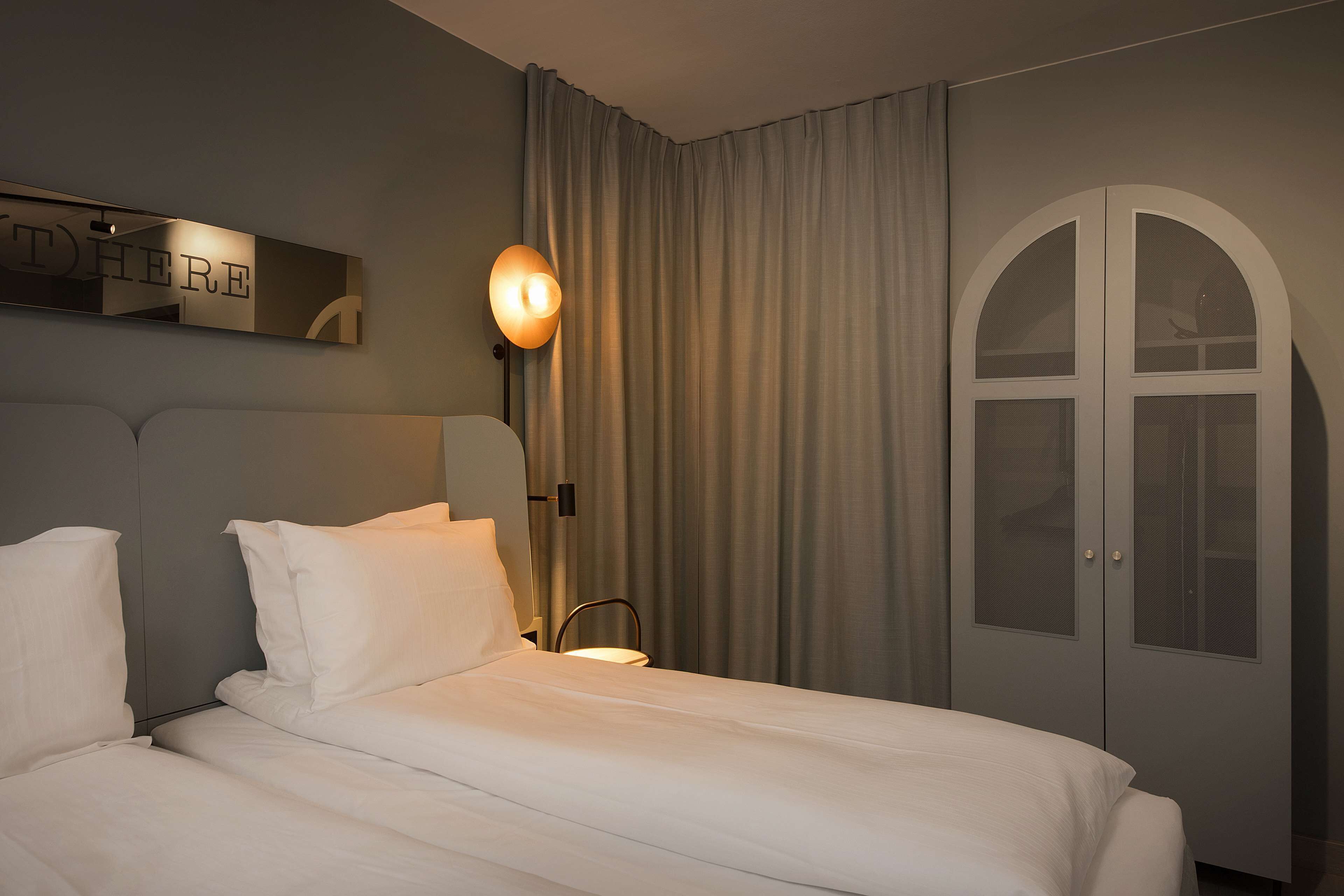 Ein Hotelzimmer mit einem großen Bett, einem Schrank mit Spiegel und einer Wandleuchte.