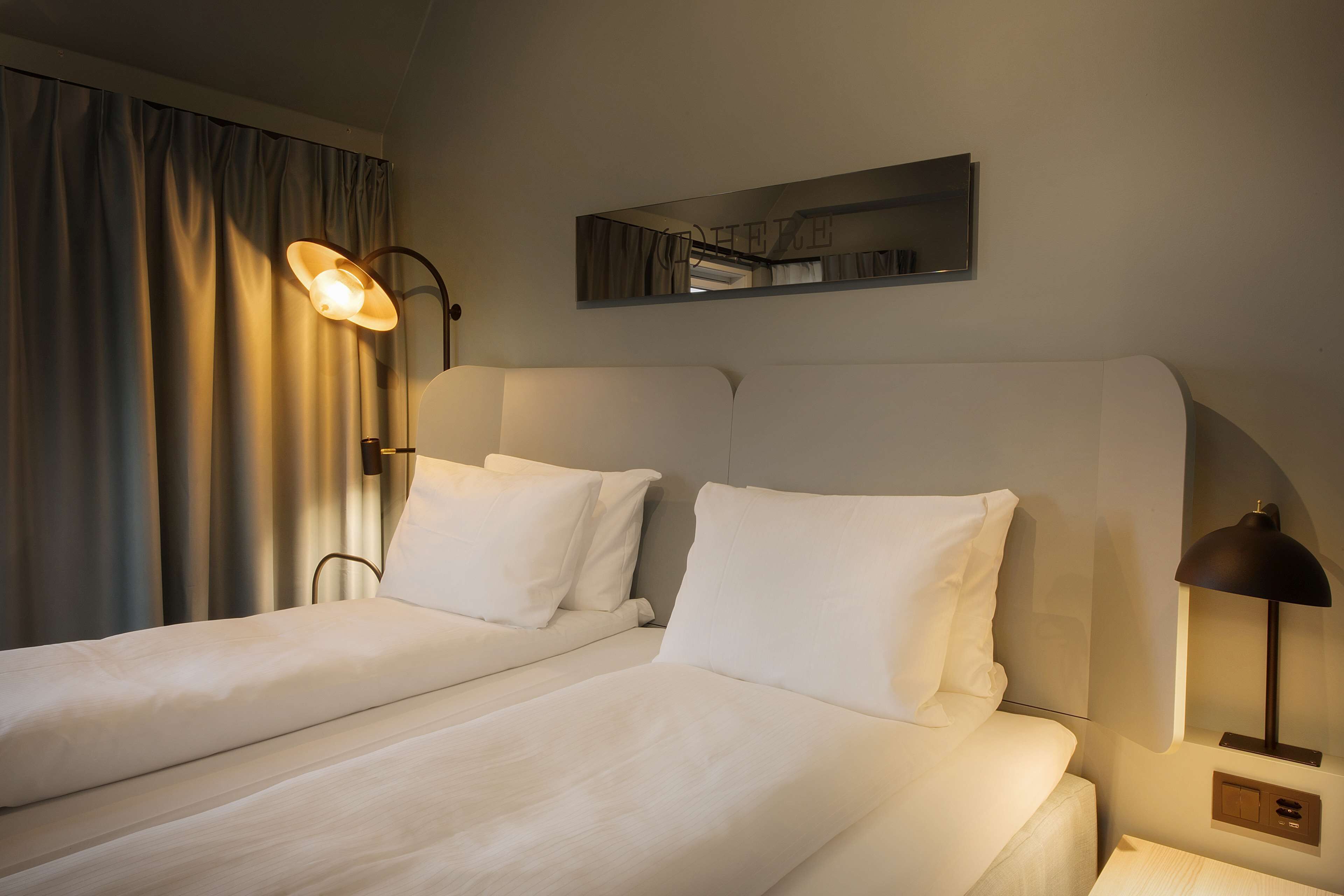 A hotel room with two beds, a large mirror, and a bedside lamp.