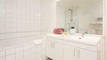 Un baño moderno con azulejos blancos, un espejo grande, una bañera y un lavabo doble.