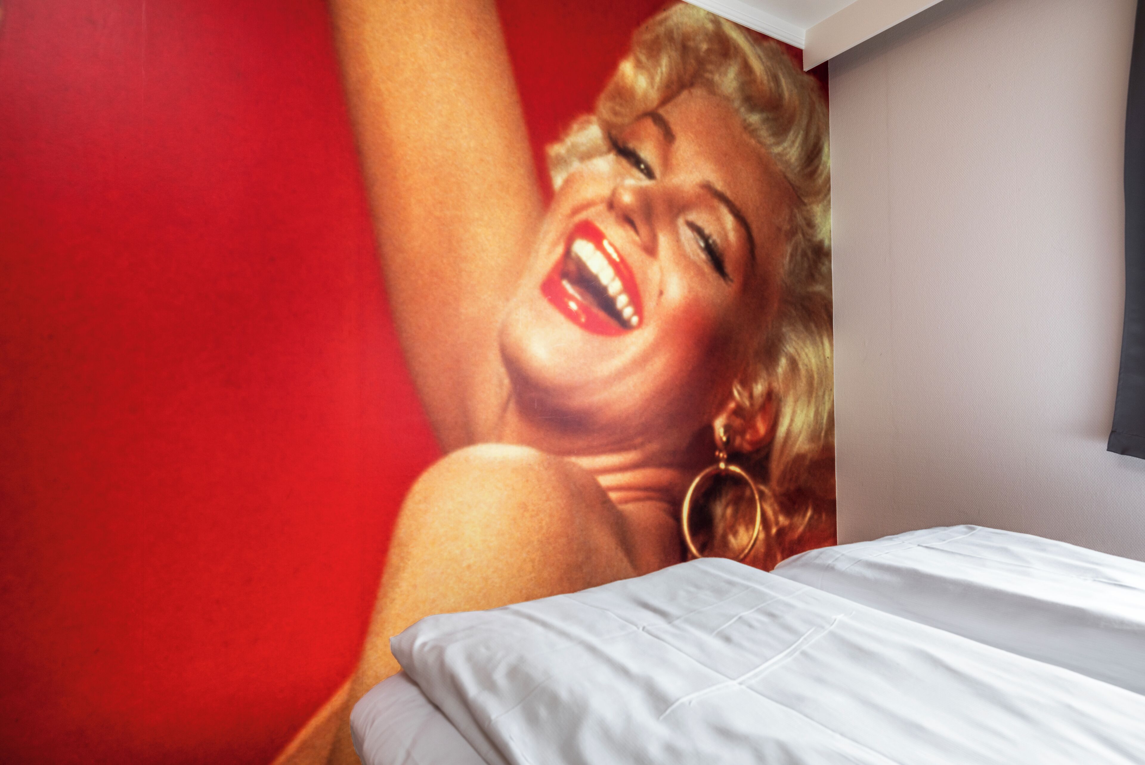 A bed with white bedding and a red wall in the background.