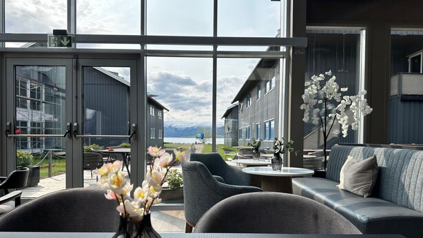 A modern interior with large windows, a seating area with sofas and chairs, and a vase with flowers on a table.