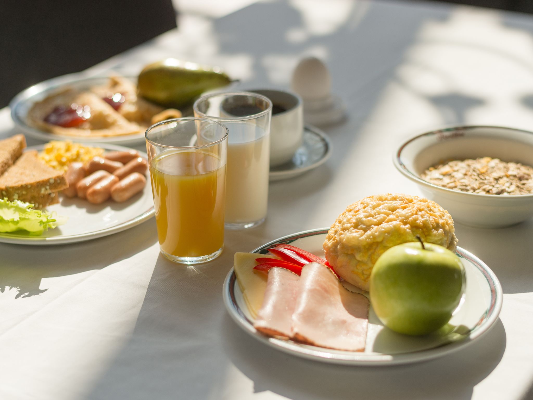 A breakfast setting with plates of food, a glass of orange juice, and a bowl of cereal.