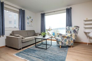 A living room with a sofa, a patterned armchair, a coffee table, and a view of the sea.