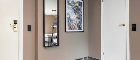 A hallway with a marble floor, a framed abstract painting, a large mirror, and a white door.