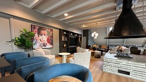 A modern living room with blue armchairs, a wooden coffee table, and a large painting on the wall.