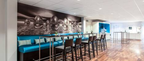 A modern bar area with a blue sofa, bar stools, and a wall mural of eggs.