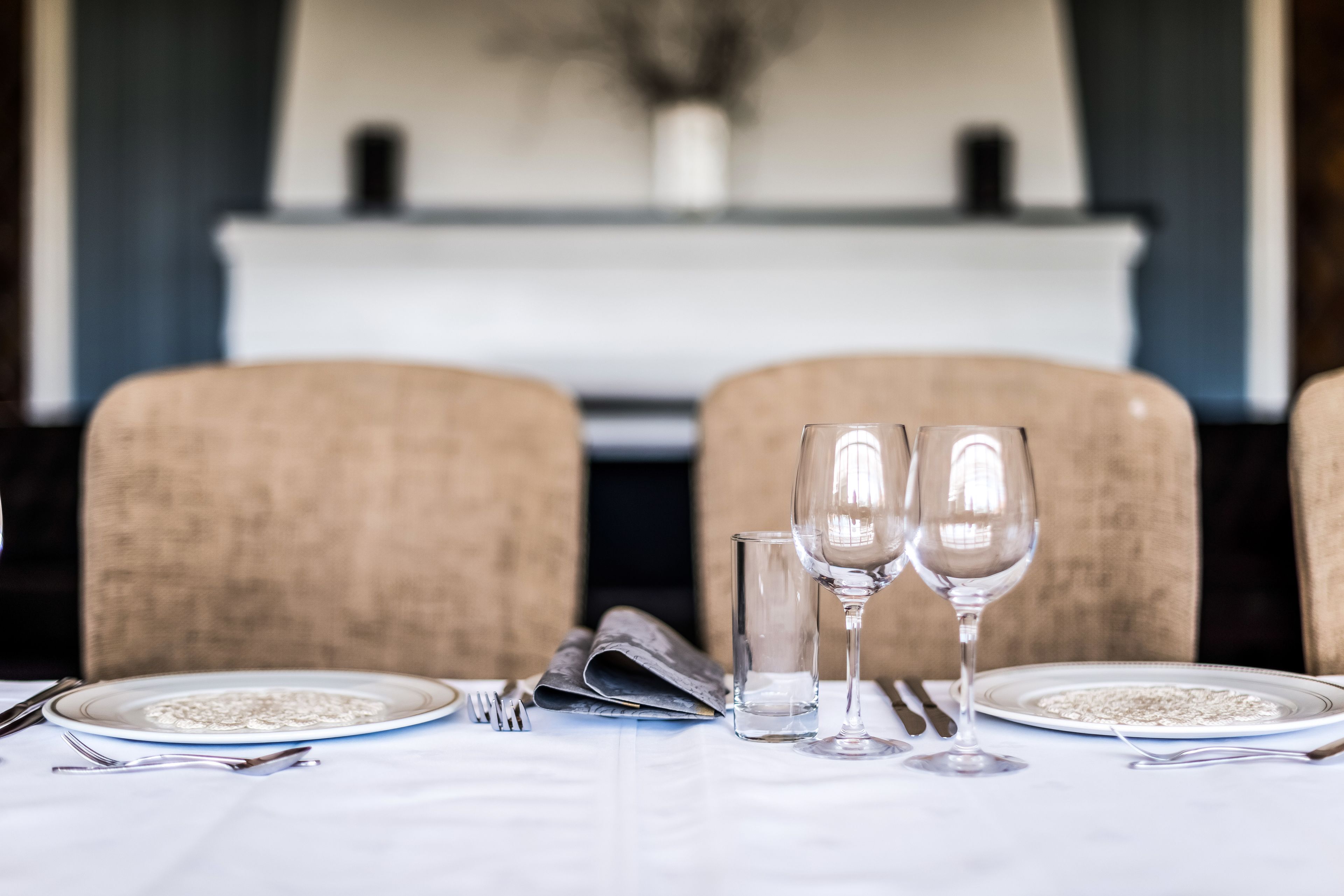 Una mesa de comedor preparada con platos, cubiertos y dos copas de vino.