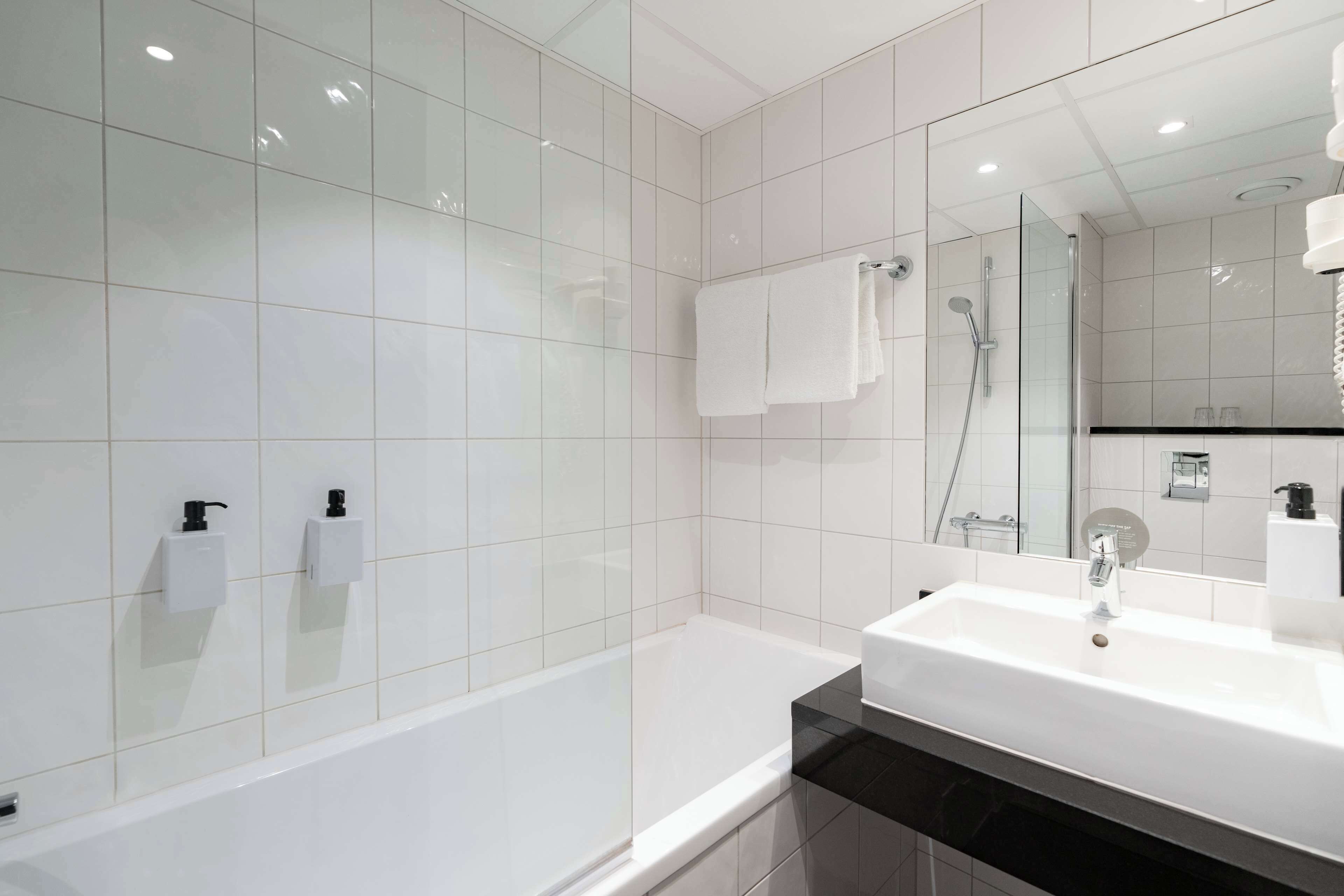 Ein modernes Badezimmer mit einer weißen Badewanne, einem großen Spiegel und einem Waschbecken mit schwarzer Ablagefläche.
