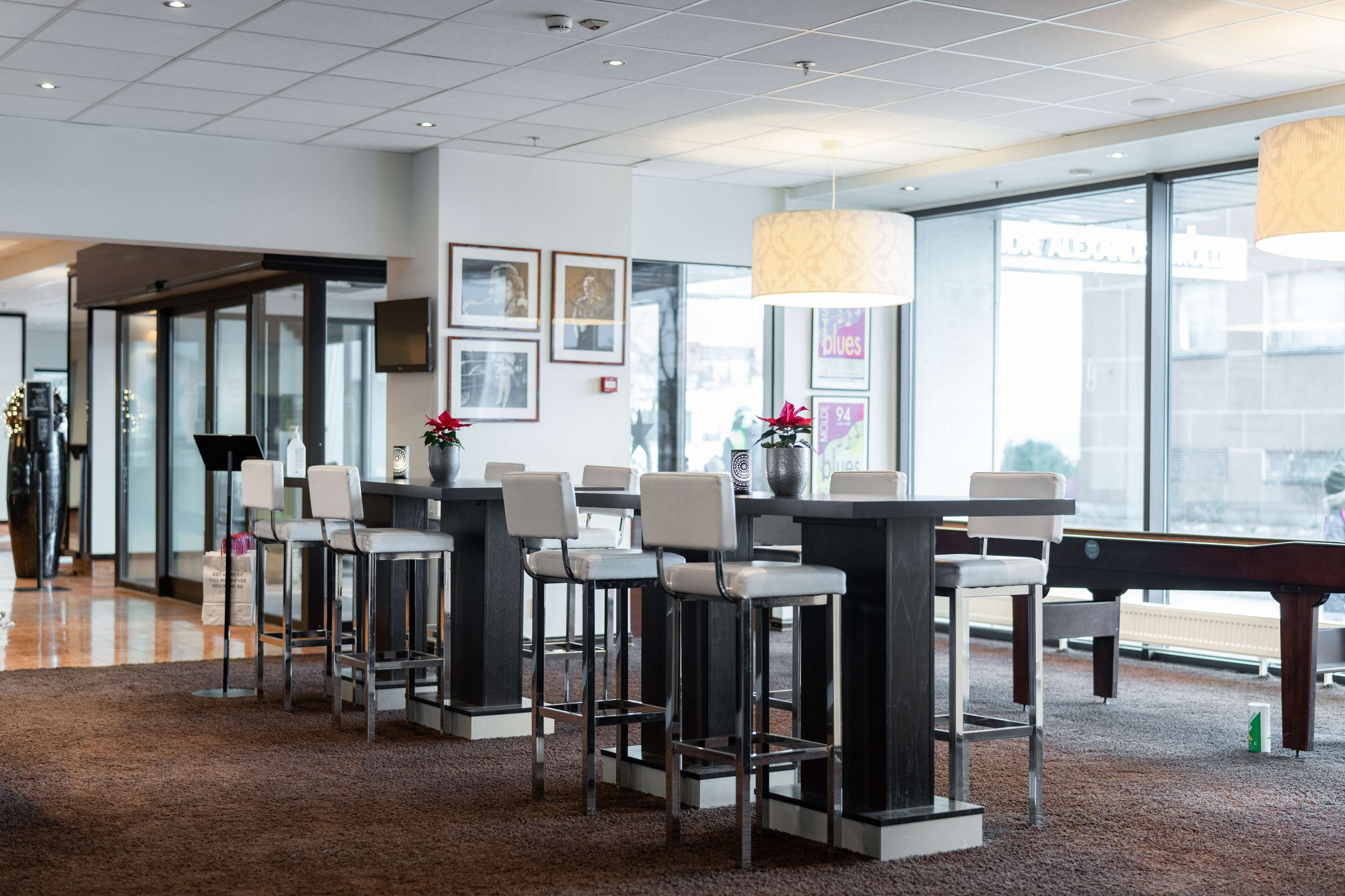 A modern bar area with high stools, a pool table, and large windows offering a view of the city.