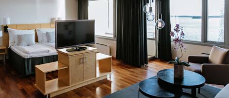 Habitación de hotel con cama, televisor, escritorio, silla y vista al agua.