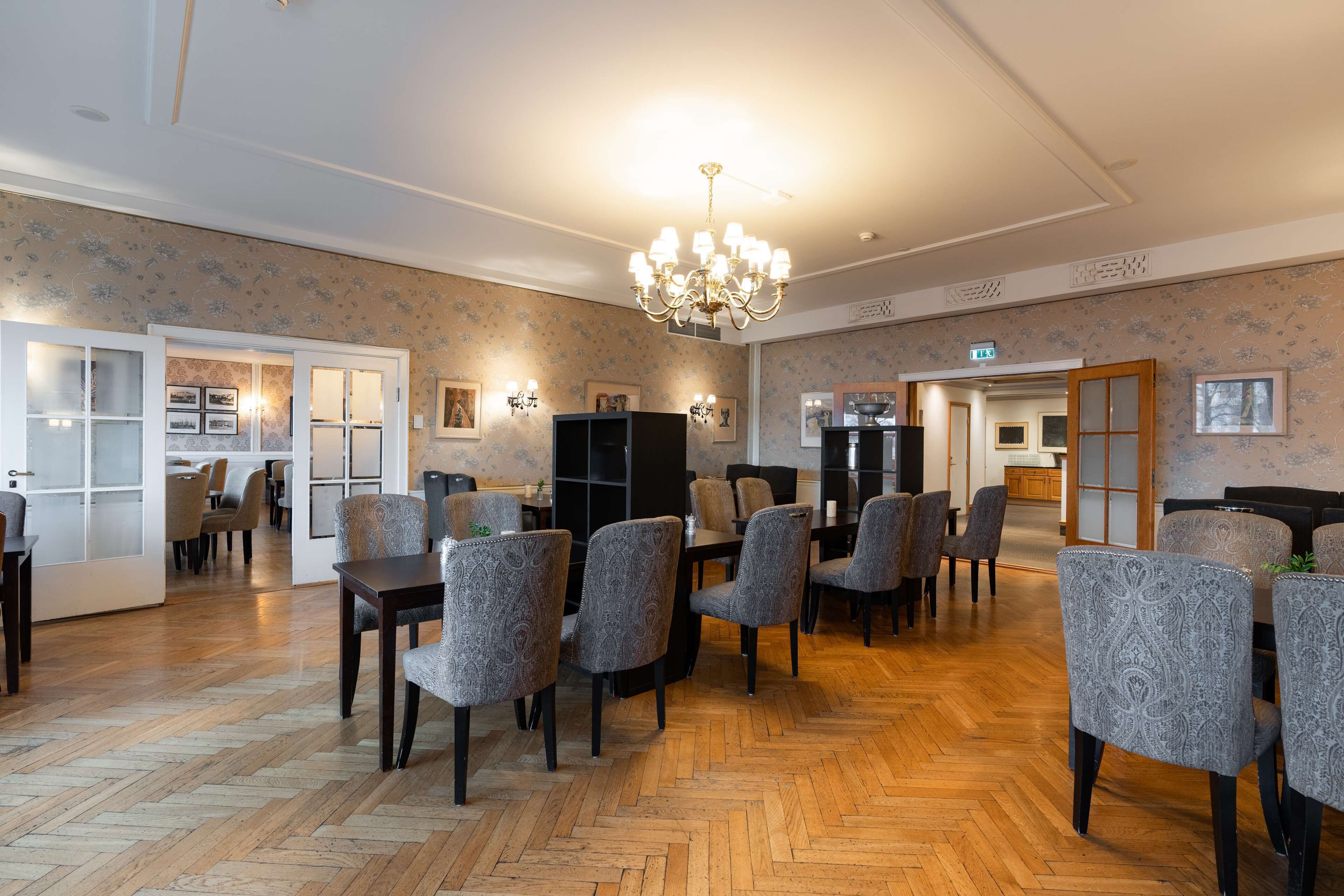 A spacious room with patterned wallpaper, wooden flooring, and a chandelier.