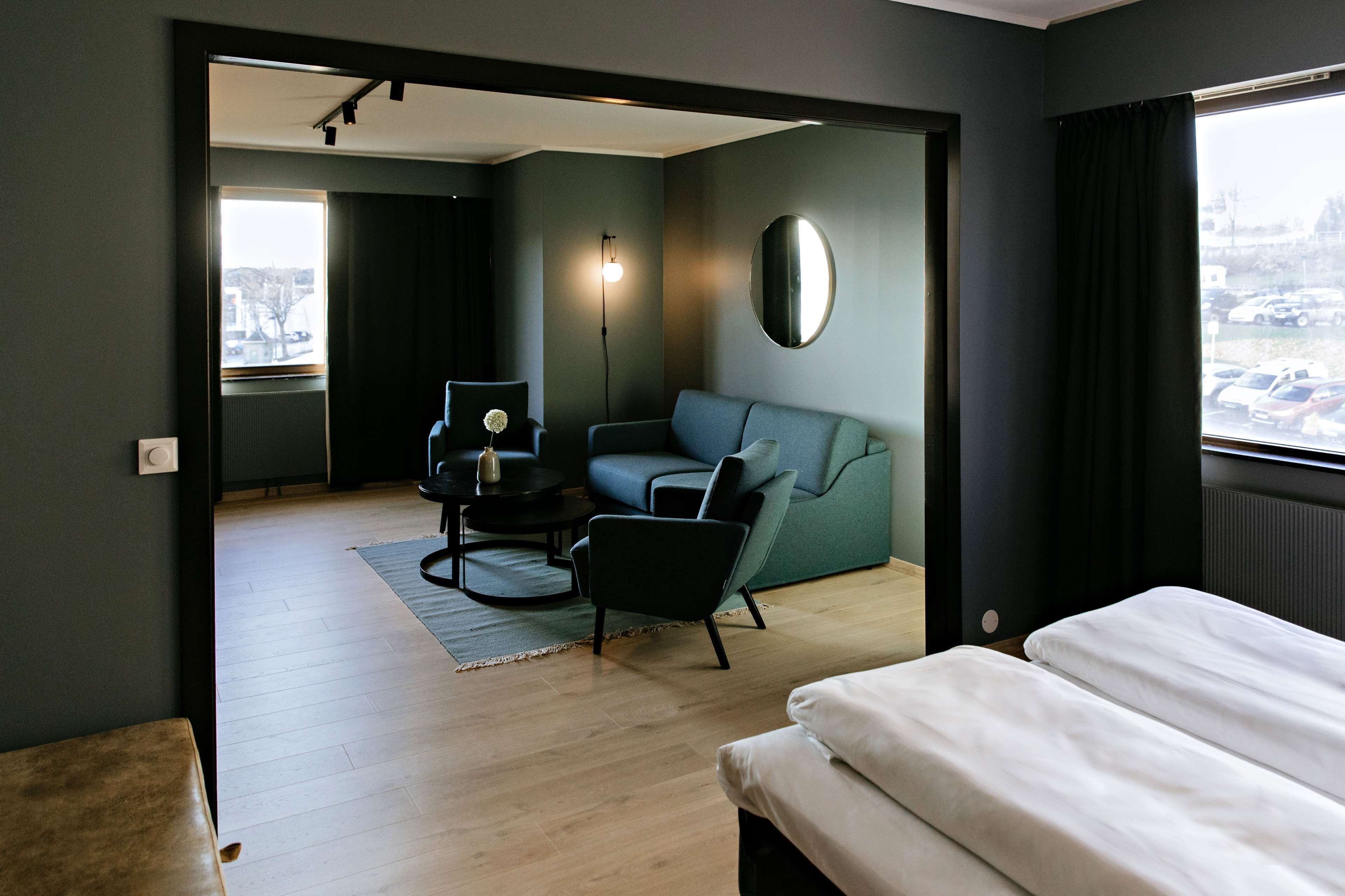 A modern hotel room with a sofa, a small table, a chair, and a bed.