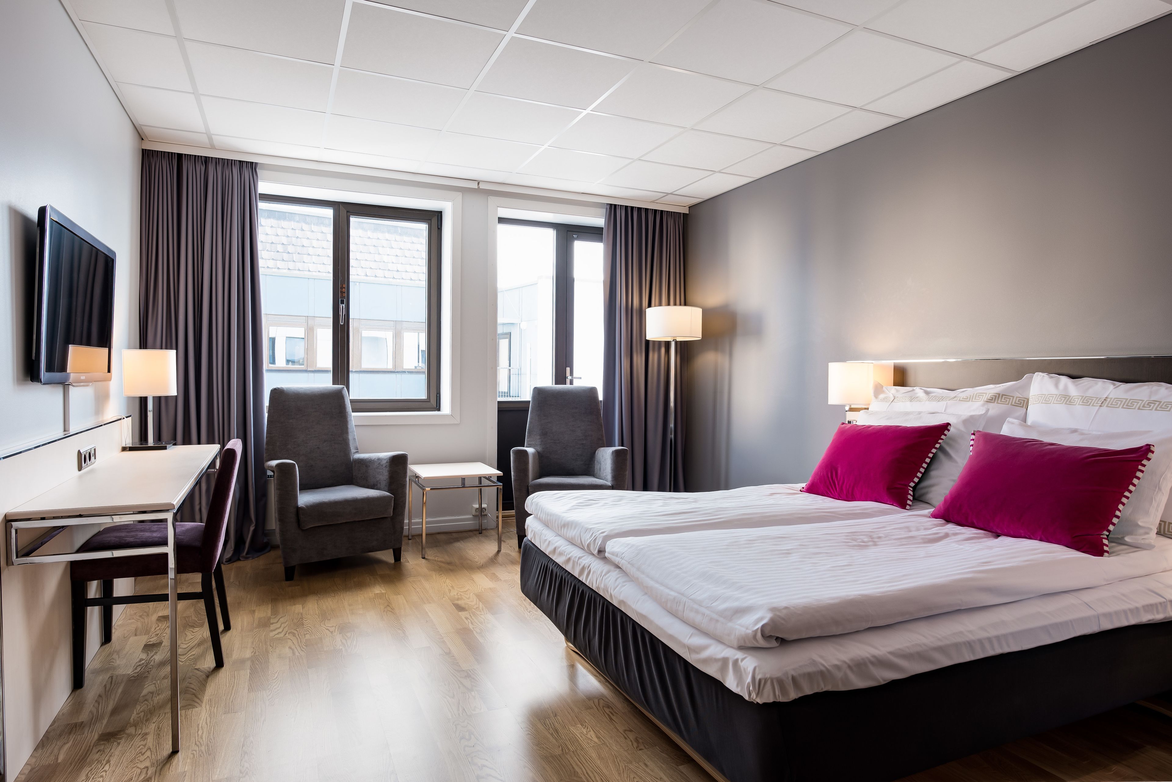 A hotel room with a bed, two chairs, a desk, and a TV.