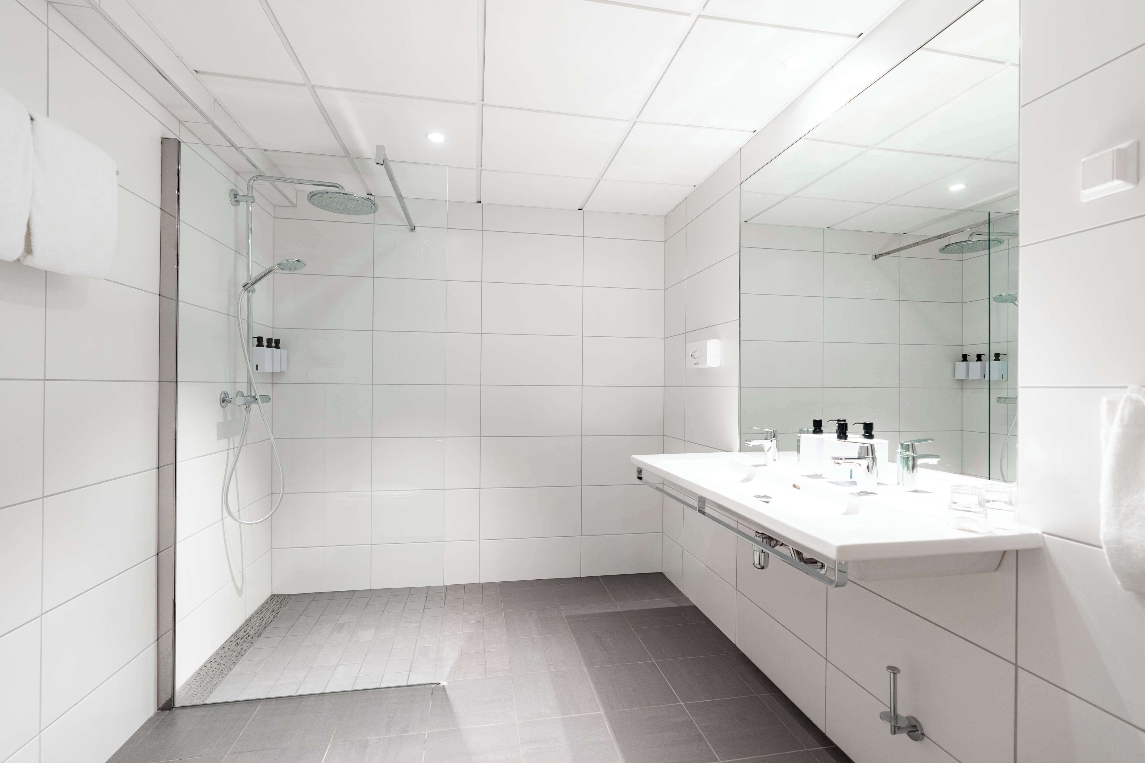 A modern bathroom with a glass-enclosed shower, a large mirror, and a vanity with toiletries.