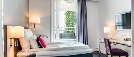 A hotel room with a bed, a desk, a chair, a TV, and a window with curtains.