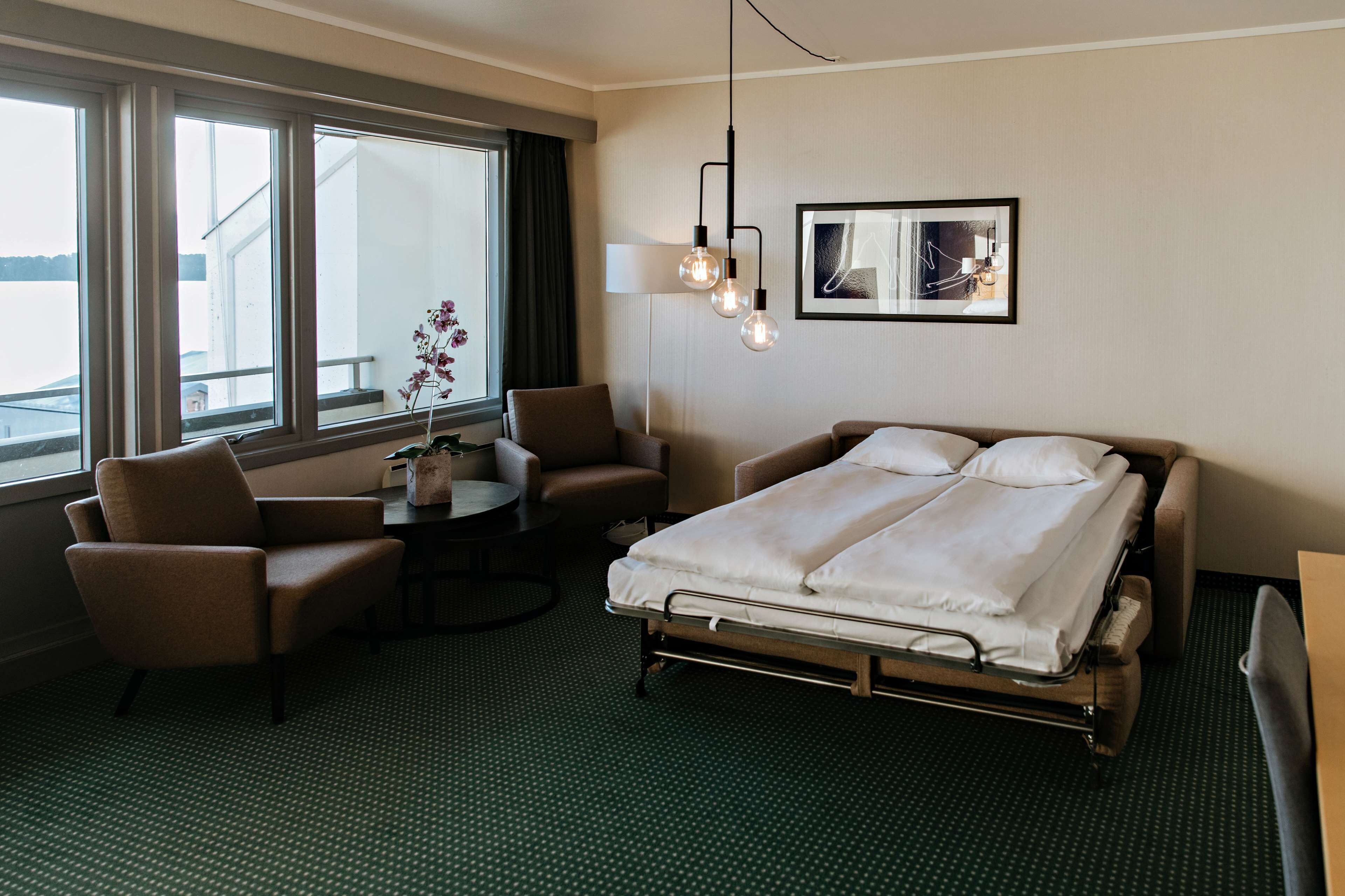 A hotel room with a bed, two armchairs, a small table, and a window with a view.