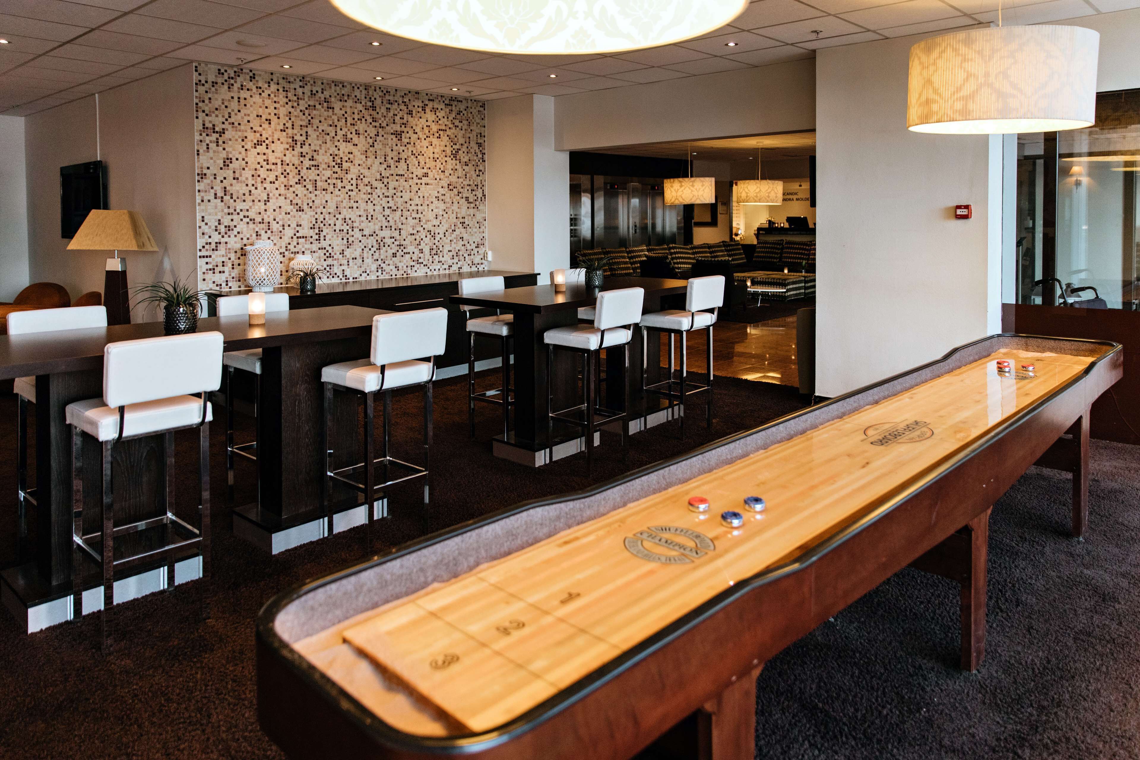A bar area with a shuffleboard table, bar stools, and a patterned wall.