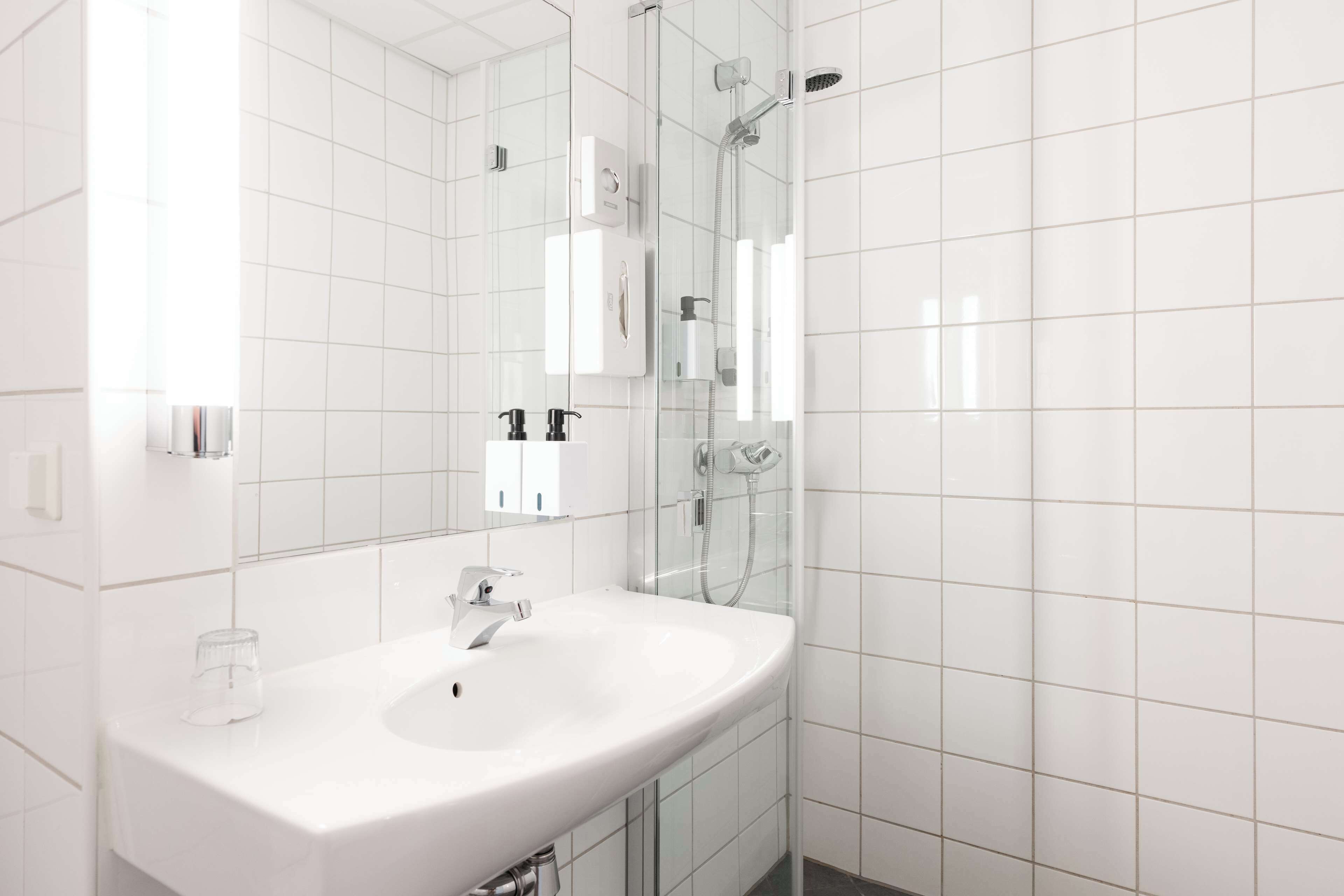 Un baño moderno con un lavamanos blanco, cabina de ducha de vidrio y un espejo grande.