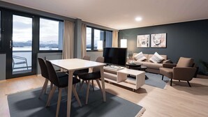 A modern living room with a dining area, a sofa set, and a TV. Large windows offer a view of a body of water and mountains. - Scandic Alexandra Molde (Molde)