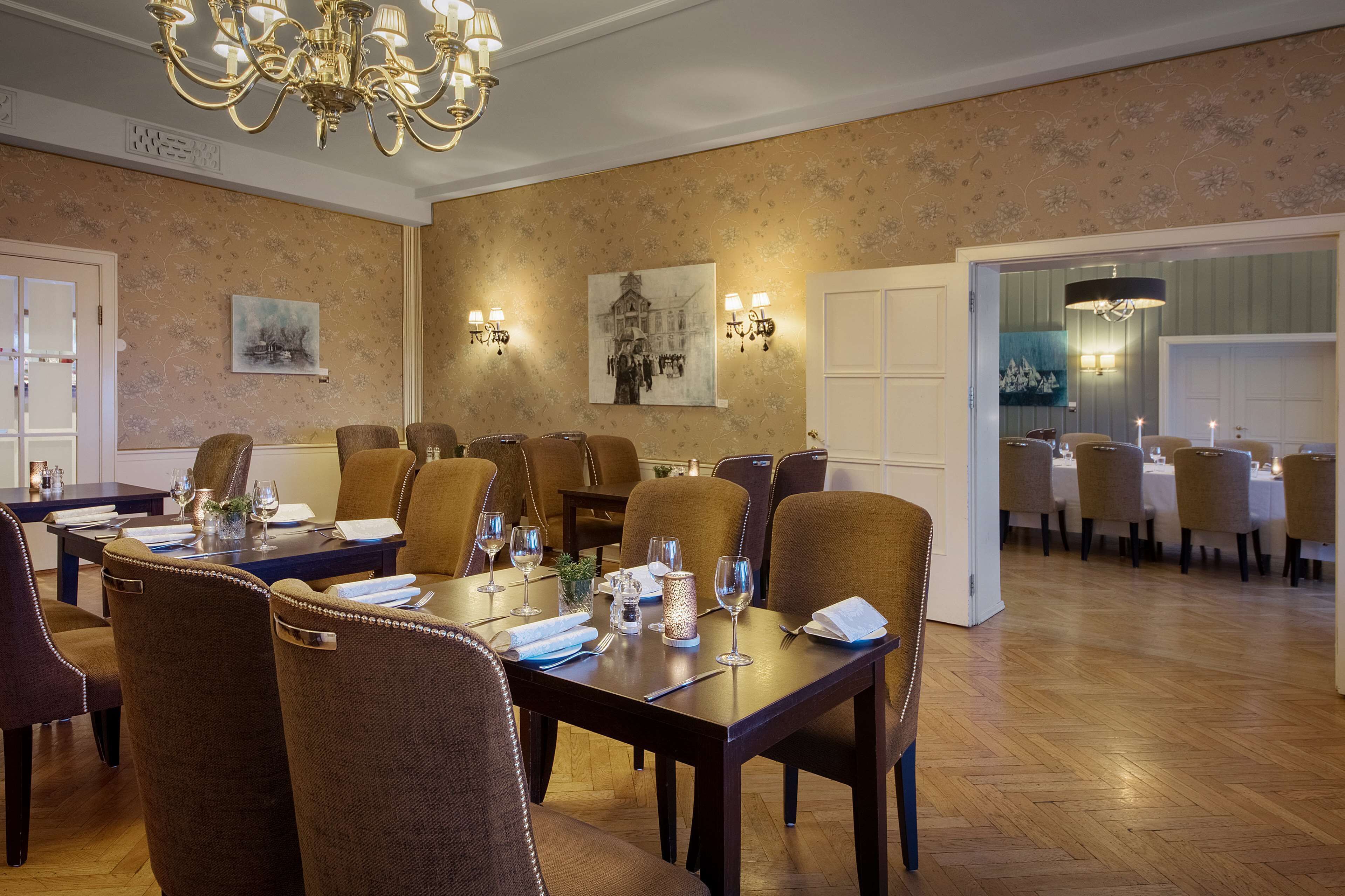 A dining area with a long table set for a meal, surrounded by chairs, with a chandelier above and wall-mounted lights.