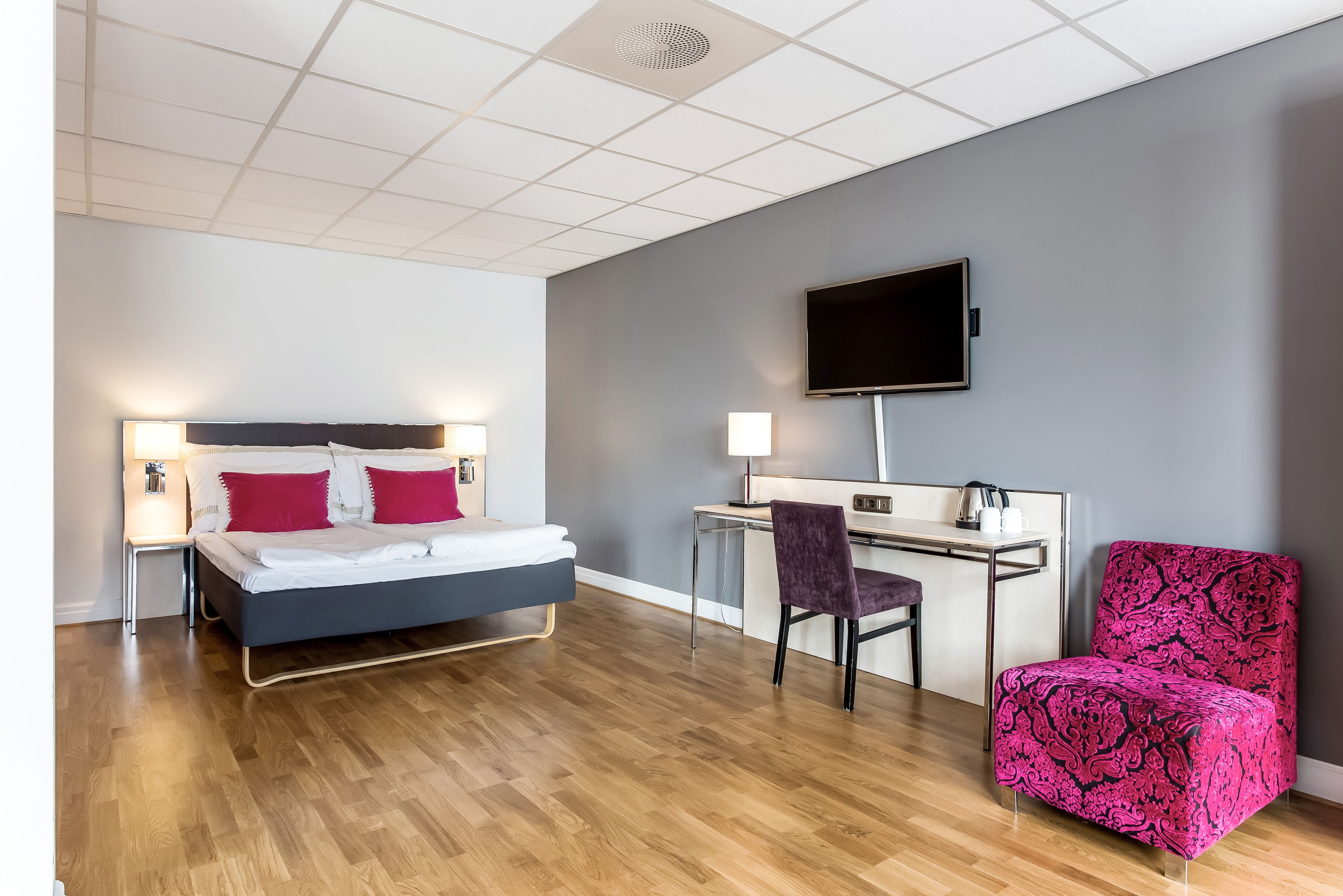 Ein modernes Hotelzimmer mit Bett, Schreibtisch, Sessel und Fernseher.