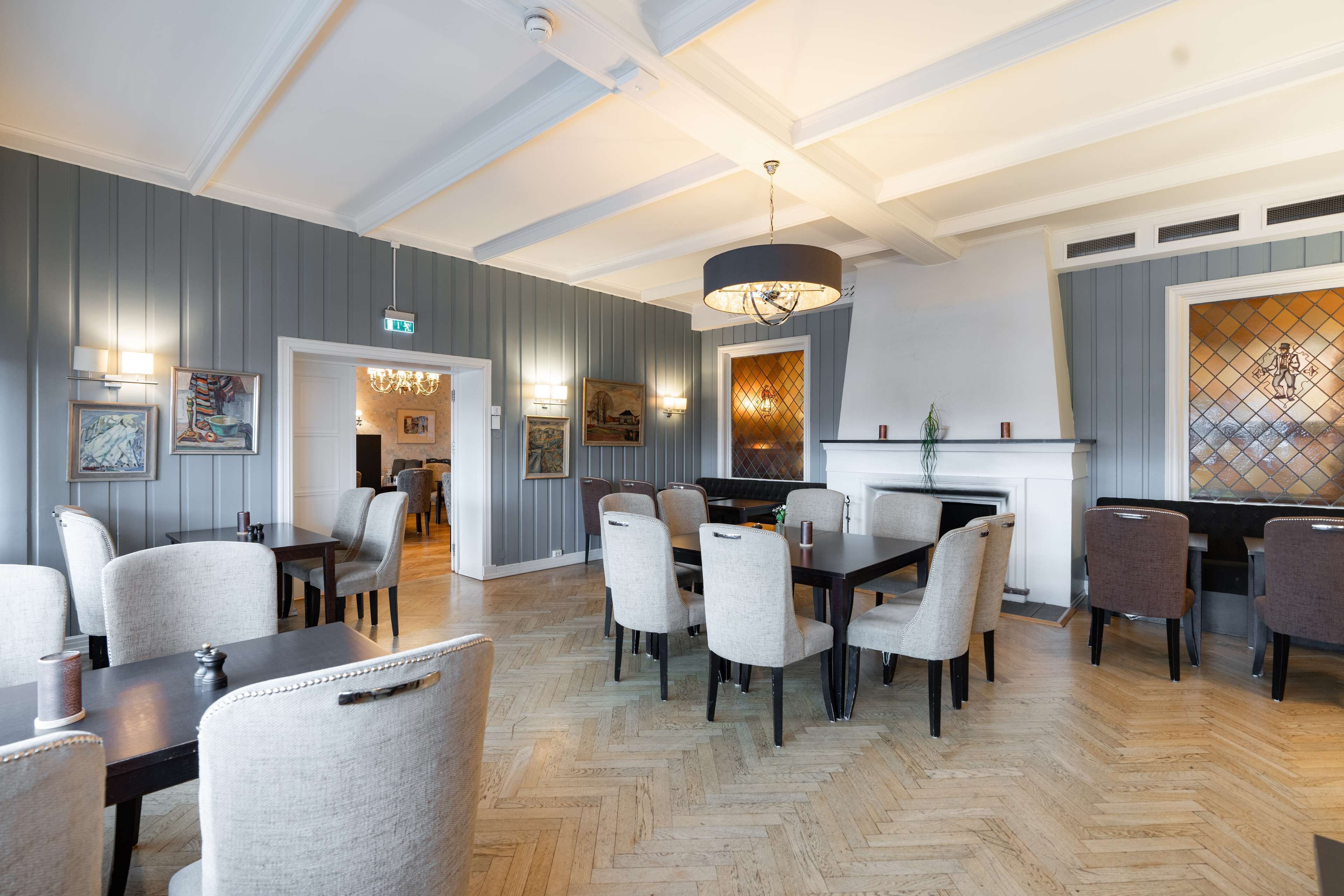 A dining area with a herringbone wood floor, grey paneled walls, and a chandelier.