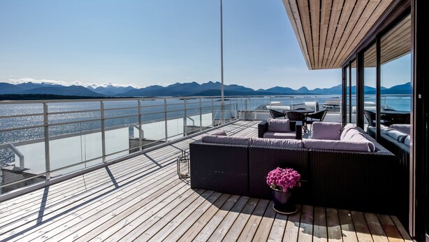 A deck with a sofa, a table, and chairs, overlooking a body of water and mountains. - Scandic Alexandra Molde (Molde)