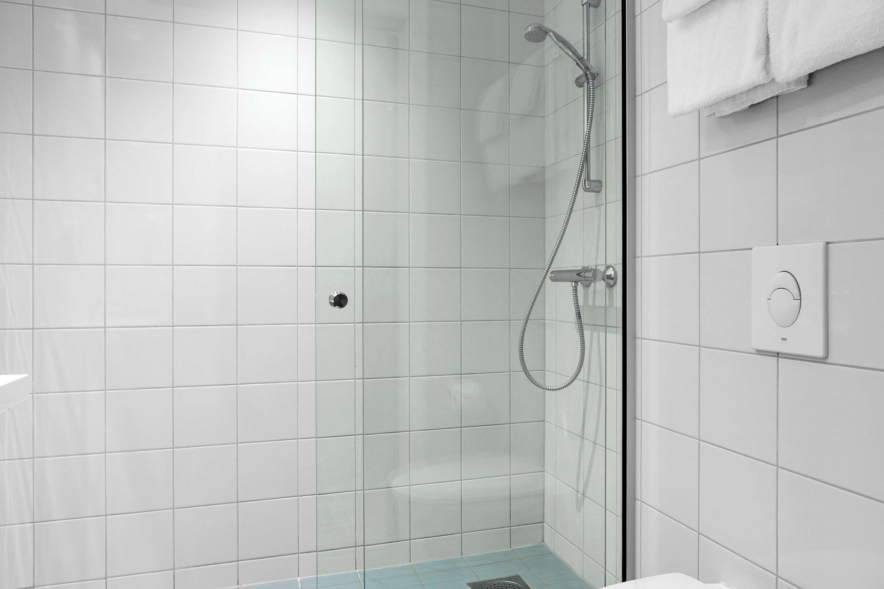 A modern bathroom with white tiles, a glass shower enclosure, and a visible control panel.