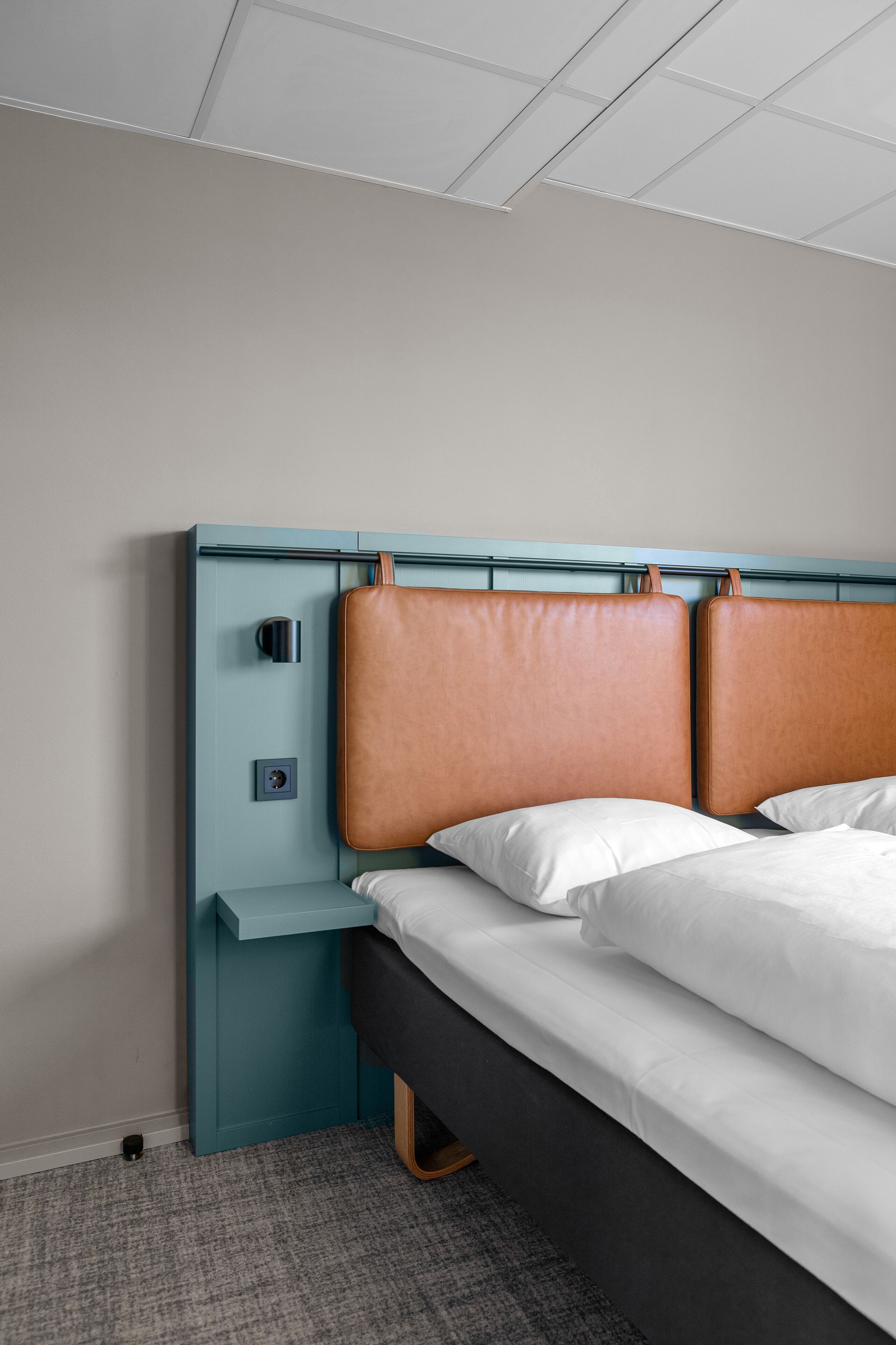 Een hotelkamer met een bed, nachtkastje en een bedieningspaneel aan de muur.