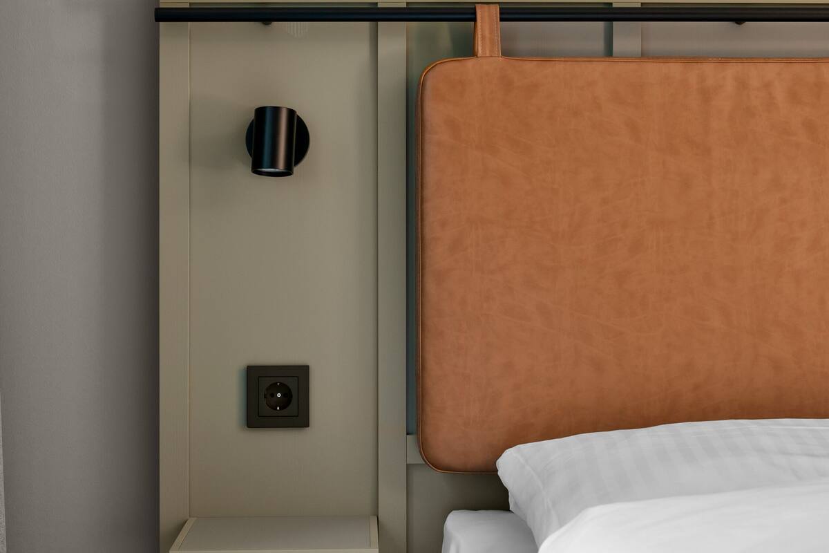 A bed with white bedding, a headboard, a bedside table, and a wall-mounted light fixture.