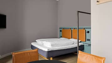 Una cama individual con cabecera, una mesita de noche y una silla en una habitación con pared gris y un televisor montado.