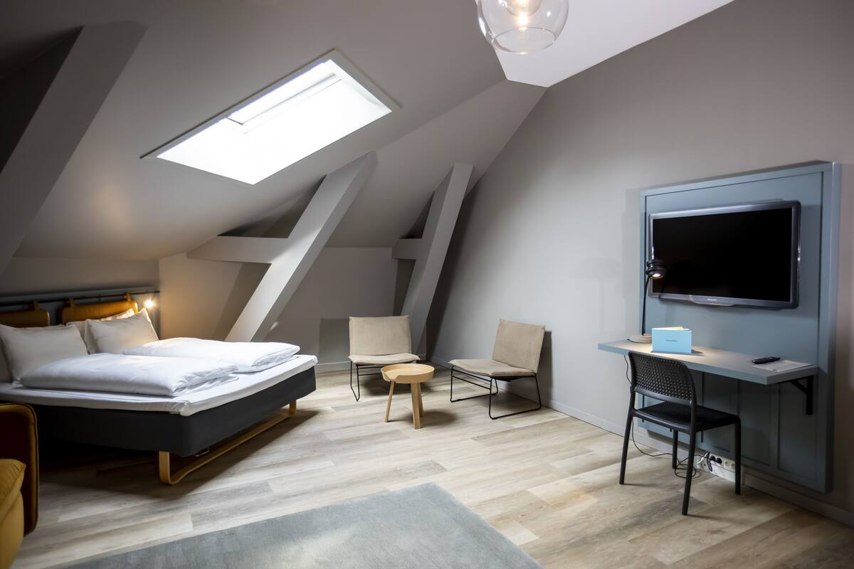A modern bedroom with a skylight, a bed, a desk, and a TV.