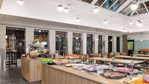 A modern cafeteria with a long counter displaying various food items, surrounded by tables and chairs. - Comfort Hotel Børsparken (Oslo)