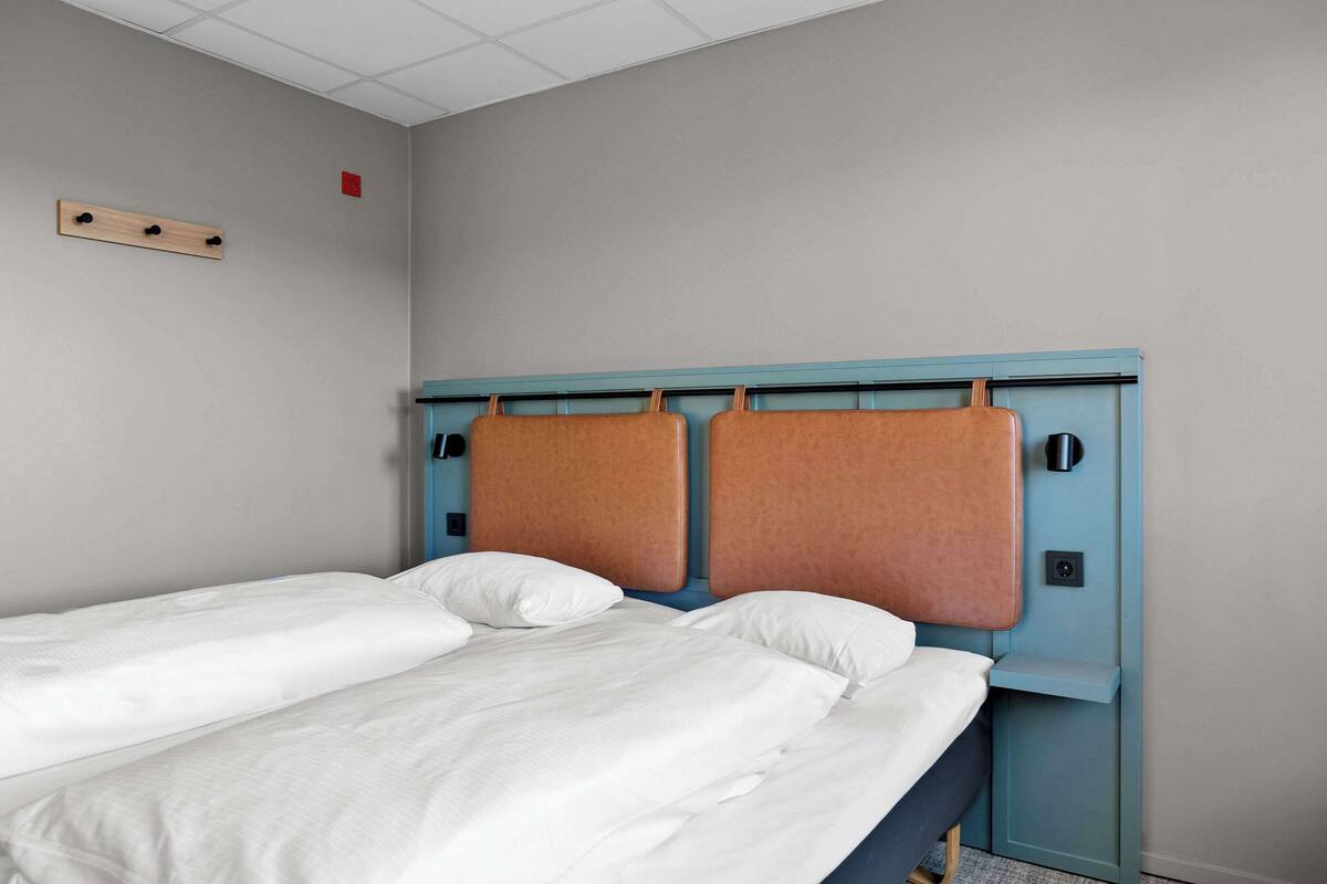 A double bed with a blue headboard, white bedding, and a small shelf on the right side.