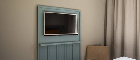 A hotel room with a bed, a chair, a television mounted on the wall, and a window with curtains.