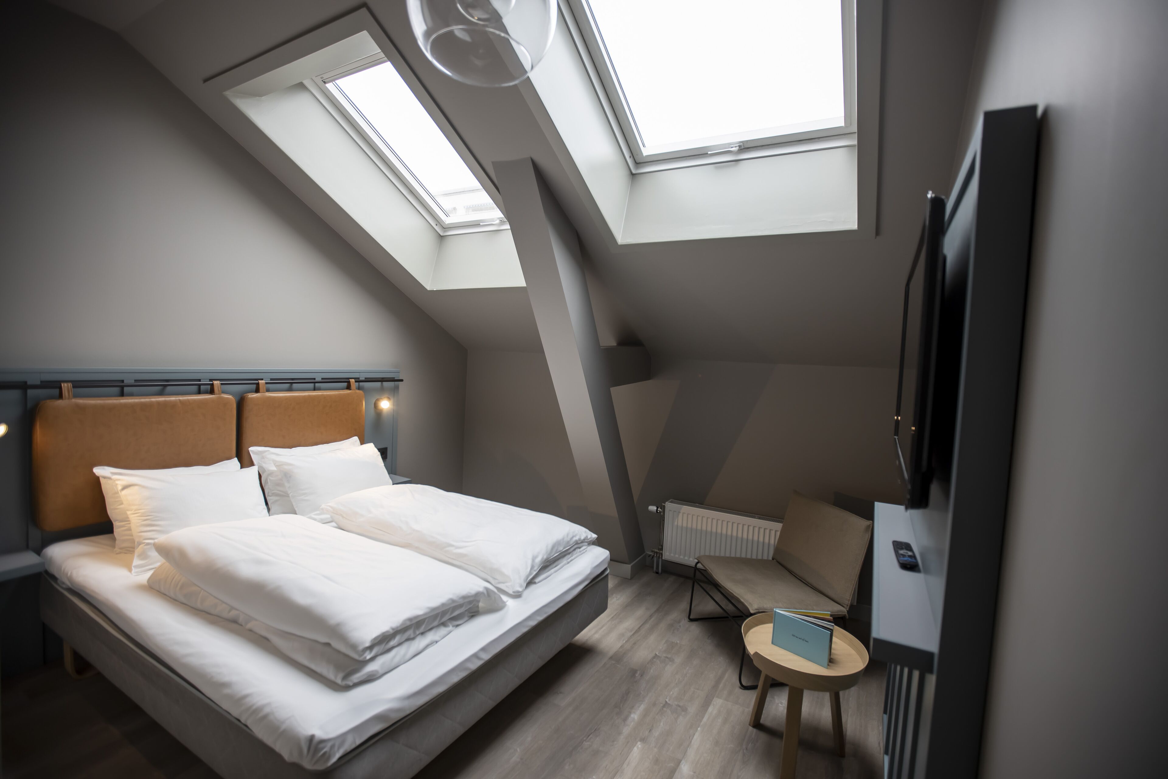 A bedroom with a bed, skylights, a TV, and a small table.