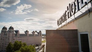 A hotel sign with the name "COMFORT HOTEL" against a backdrop of a large building with multiple towers and a partly cloudy sky. - Comfort Hotel Børsparken (Oslo)