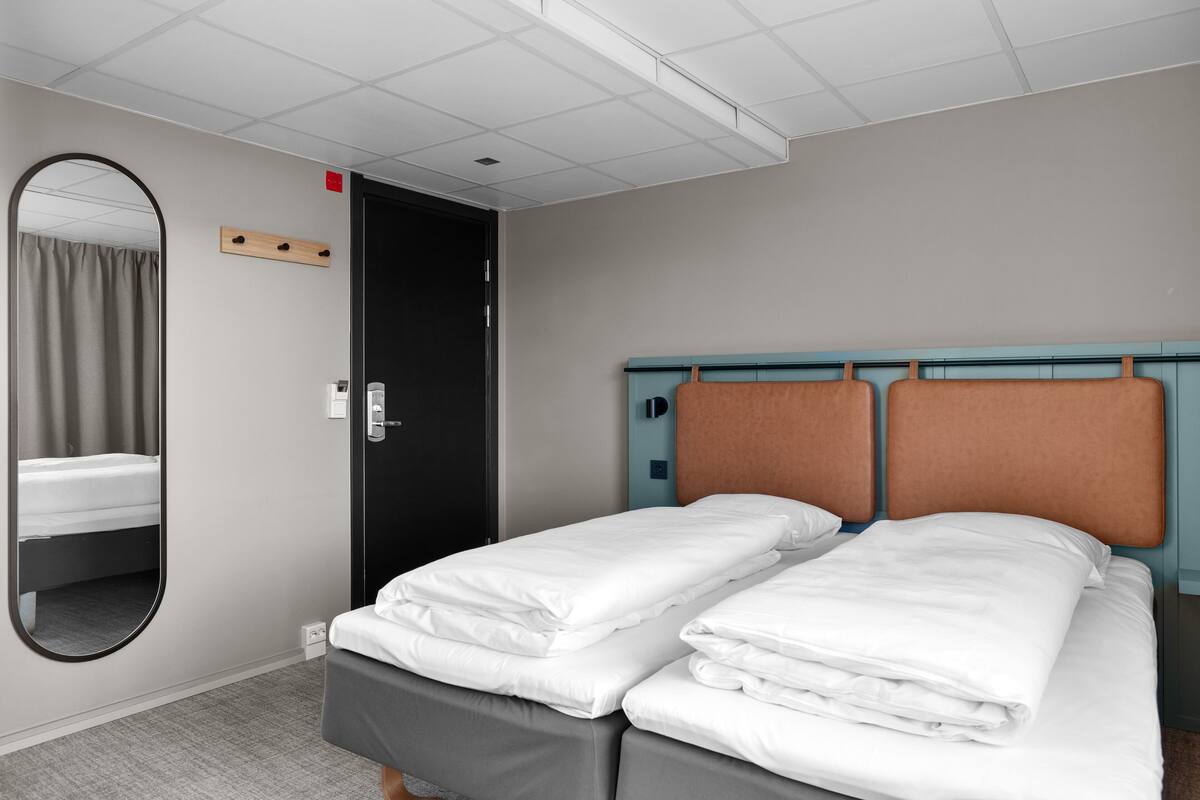 A hotel room with a double bed, a mirror, a door, and a light switch on the wall.