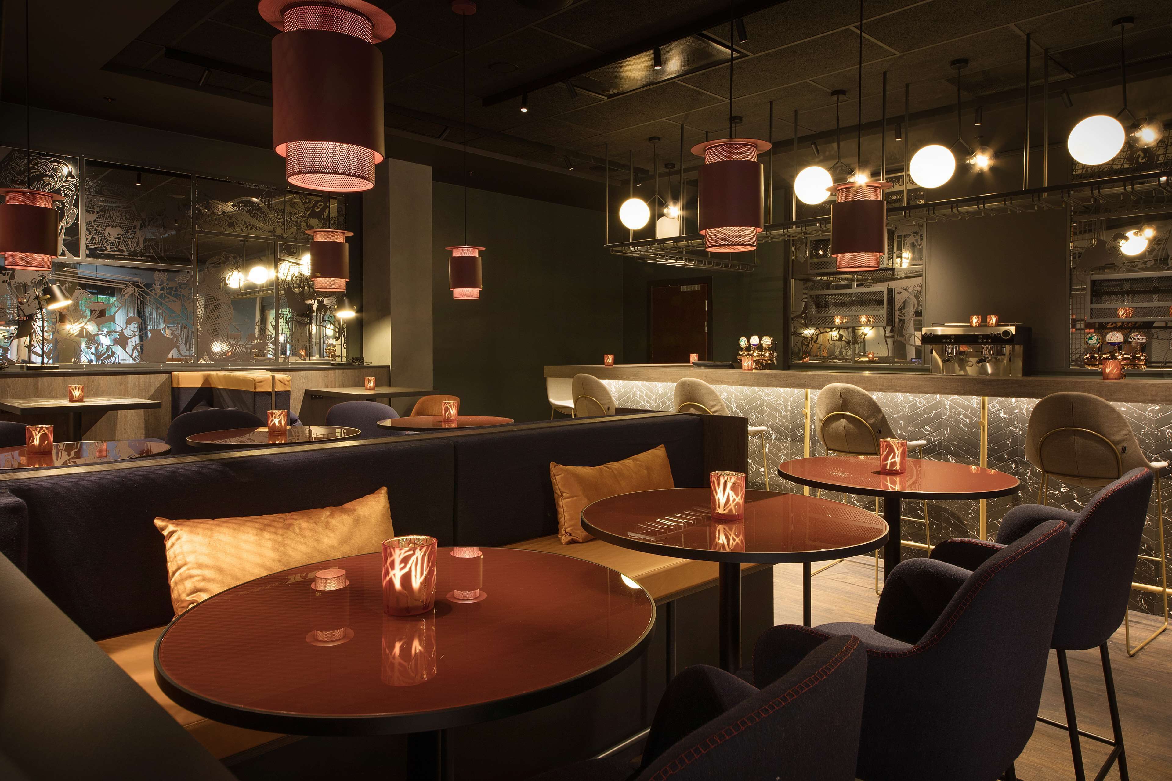 Un área de bar moderna con mesas redondas, asientos acolchados e iluminación colgante.