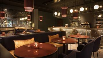 Un área de bar moderna con mesas redondas, asientos acolchados e iluminación colgante.