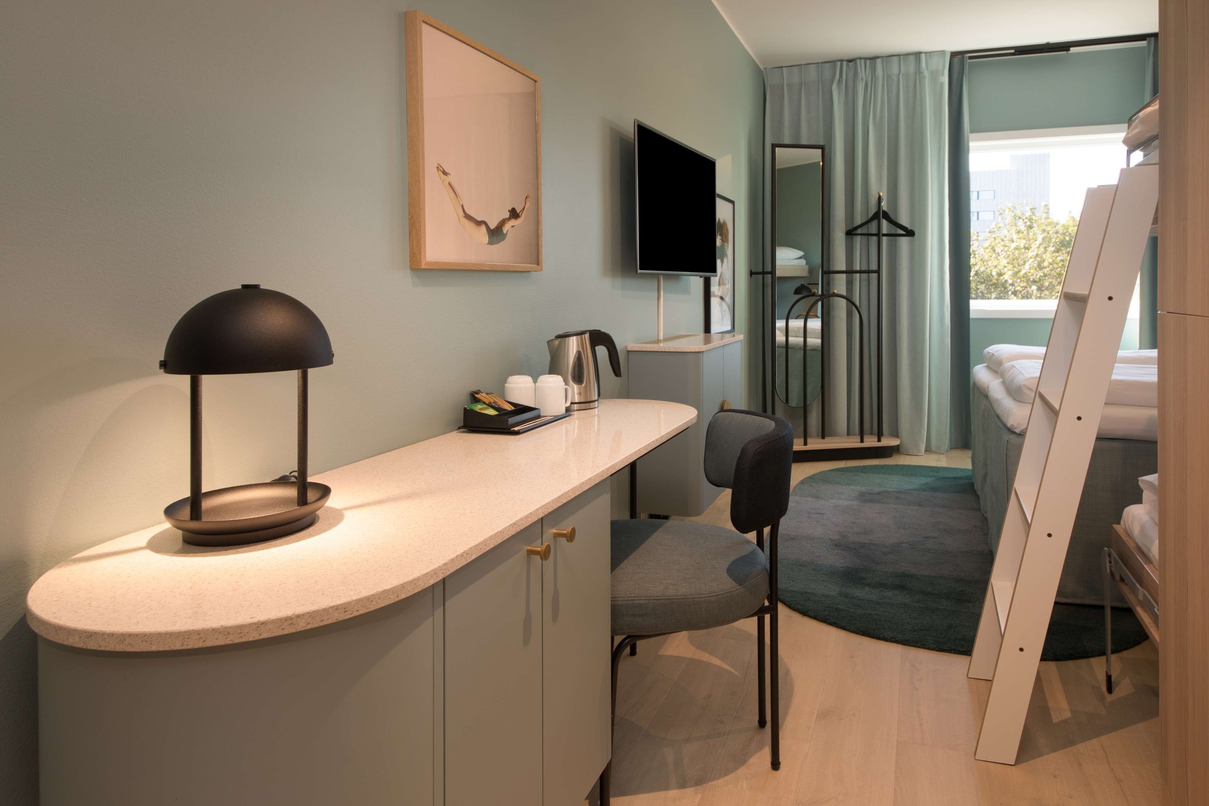 Una habitación de hotel moderna con una encimera curva, un escritorio, una silla, una cama, un televisor y una ventana con cortinas.