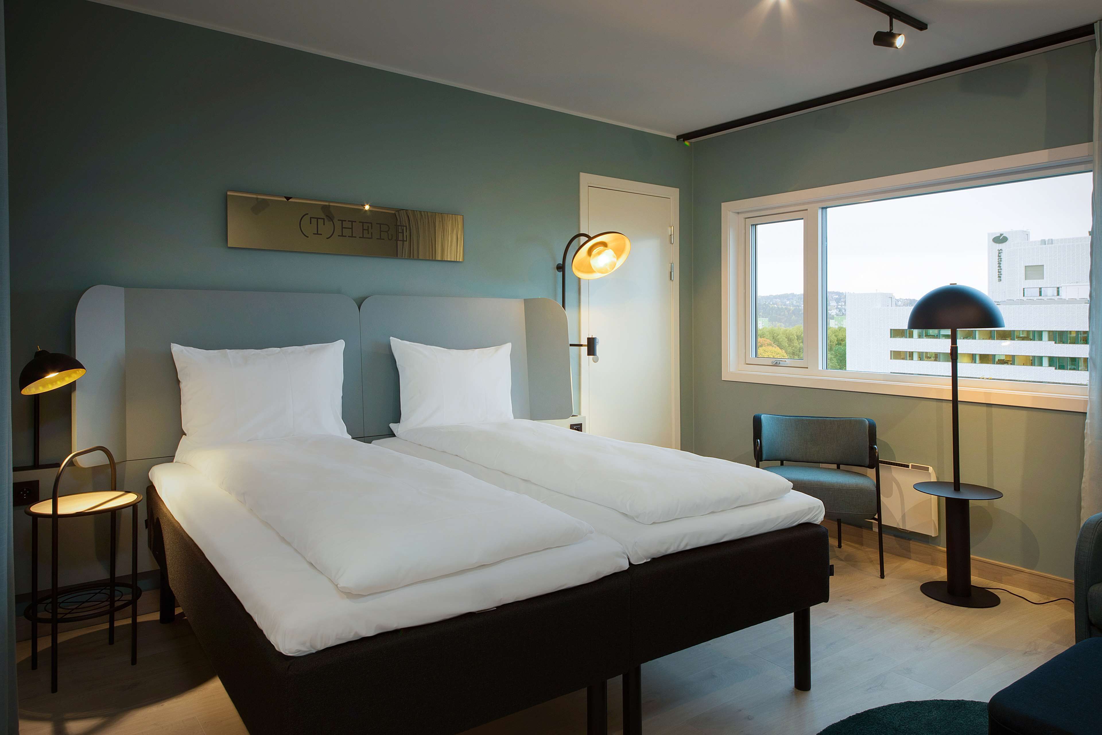 Ein modernes Hotelzimmer mit einem großen Bett, einem Schreibtisch, einem Stuhl und einem Fenster mit Blick auf Gebäude.