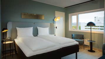 Ein modernes Hotelzimmer mit einem großen Bett, einem Schreibtisch, einem Stuhl und einem Fenster mit Blick auf Gebäude.