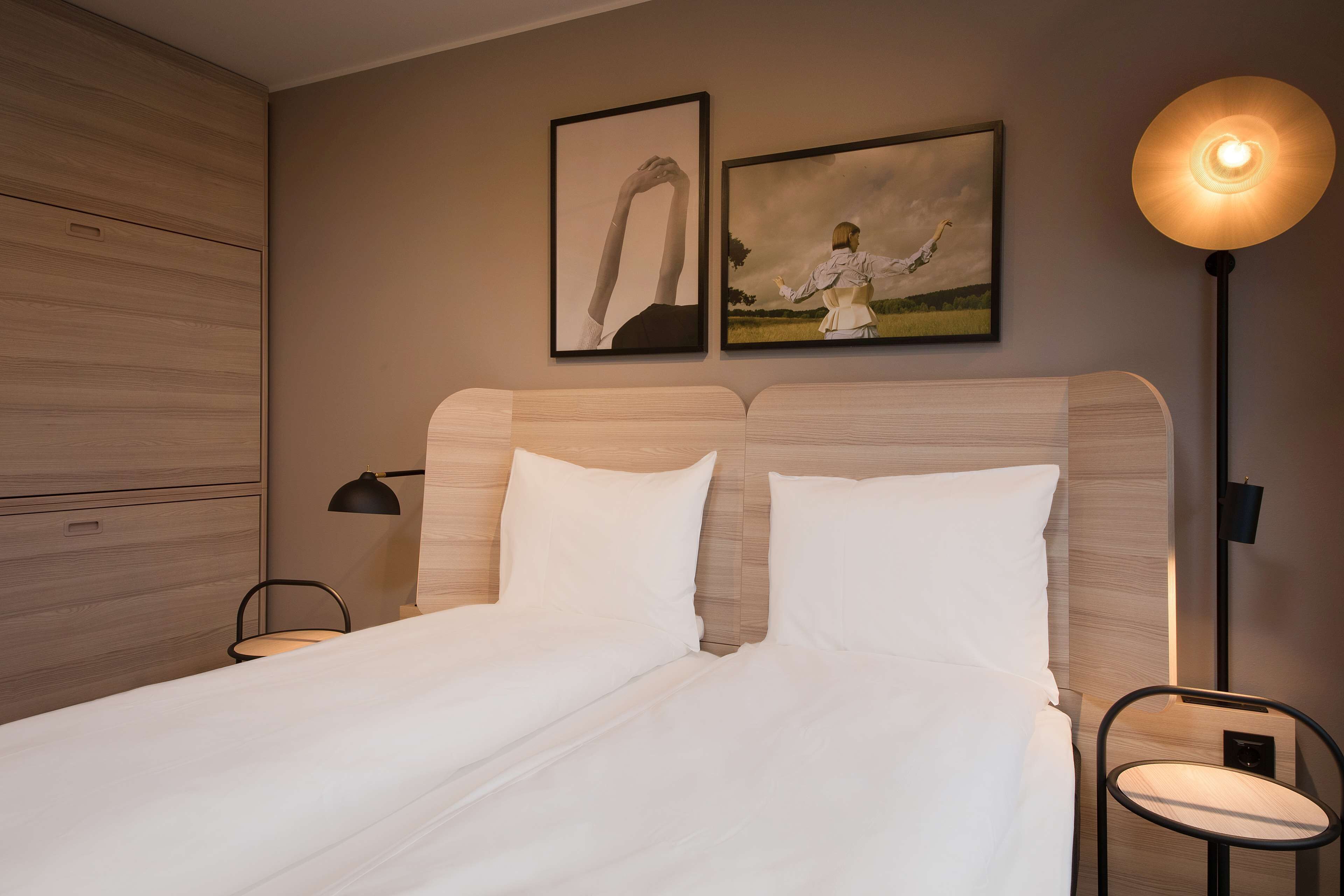 Un lit bien fait, avec du linge de lit blanc, une tête de lit et deux tableaux encadrés accrochés au mur.