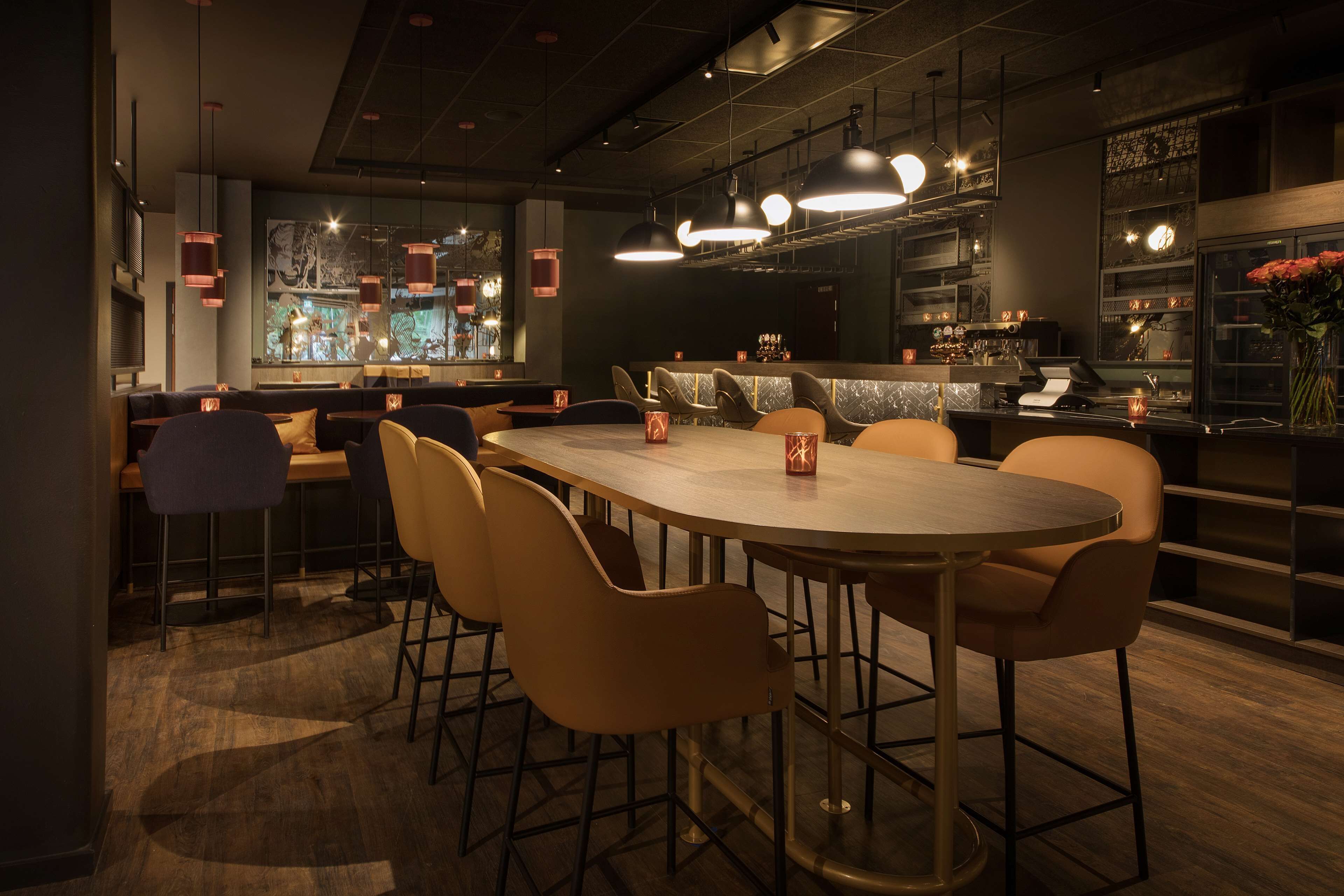 Un moderno bar con una mesa larga y varios taburetes, una barra con caja registradora y un amplio ventanal con vistas a la ciudad.